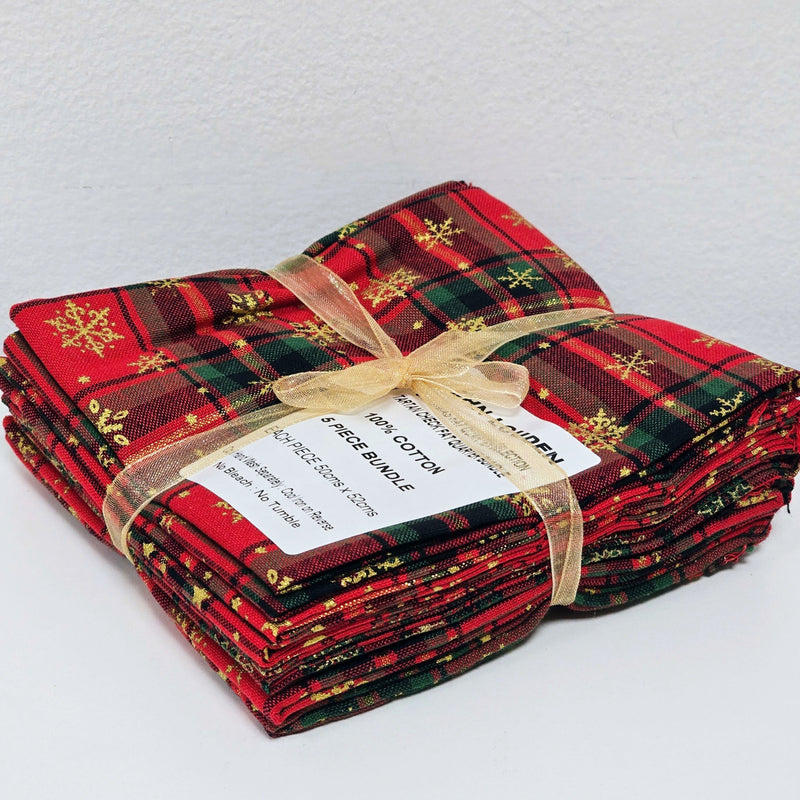 Stack of red and green plaid fabric bundles tied with a gold ribbon on a white background
